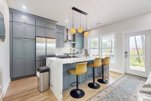 Une cuisine moderne avec des meubles gris, un réfrigérateur en acier inoxydable, un îlot en marbre et trois tabourets de bar.