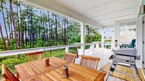 Um deck de madeira com mesa e cadeiras, com vista para uma área arborizada.