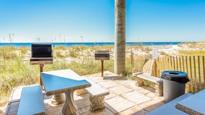 An outdoor seating area with a grill, tables, a bench, and a trash bin.