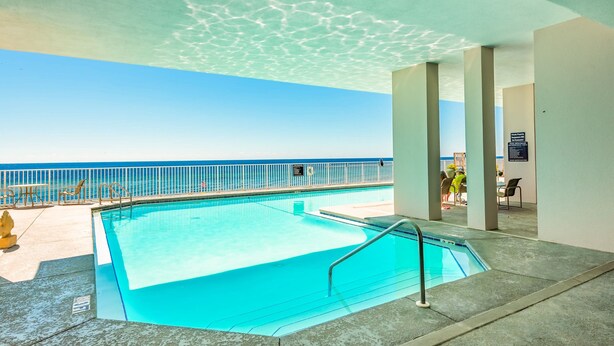 An indoor swimming pool with clear blue water, a view of the ocean, and a covered area with seating.