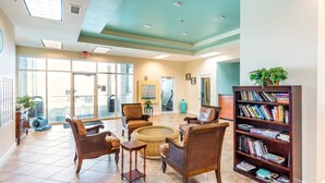 A spacious lobby with a large bookshelf, comfortable seating, and a view through the glass doors.