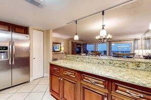A kitchen with a large island, stainless steel refrigerator, wooden cabinets, and pendant lighting. - Third-floor bright Gulf front condo with dreamy views - close to everything (Fort Walton Beach)