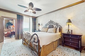 Ein geräumiges Schlafzimmer mit einem großen Bett, einem Deckenventilator, einem Nachttisch mit Lampen und Blick ins Freie.