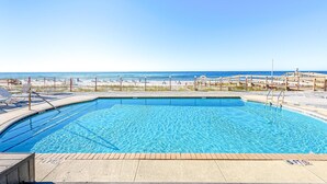 Una piscina con agua cristalina azul, rodeada por una terraza de madera y una valla metálica.