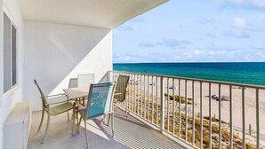 Un balcón con mesa y sillas, con vista a una playa y una barandilla.