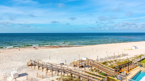 Una playa con un paseo marítimo de madera, piscina y zona de arena.