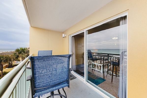 A balcony with a view of the ocean, a dining area with tables and chairs, and a blue chair. - Waterfront Gem - Shared Pool, Beach Access, Free WiFi, Washer&Dryer & Central AC (Fort Walton Beach)