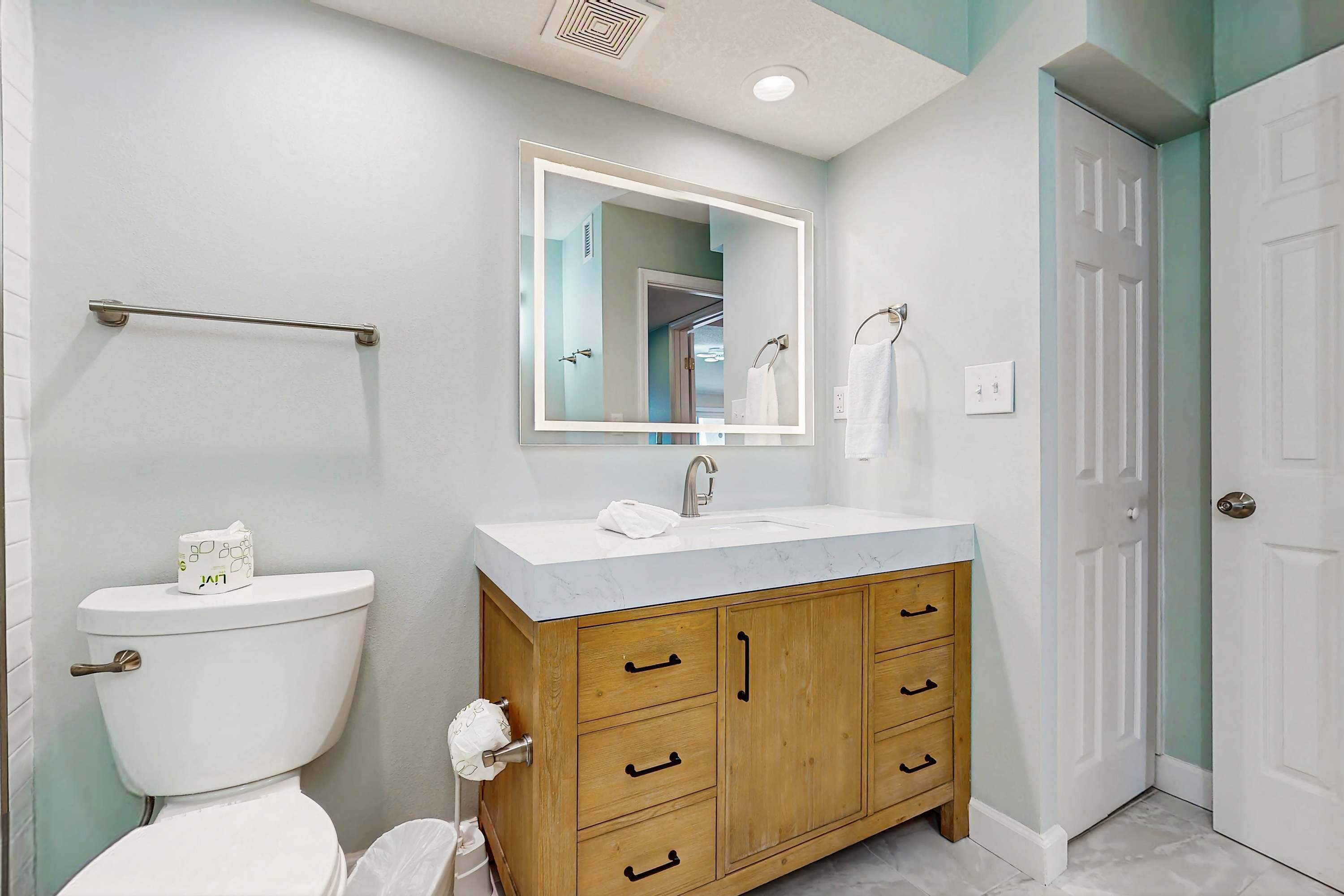 Une salle de bain comprenant des toilettes, un lavabo, un meuble-lavabo en bois et un miroir.