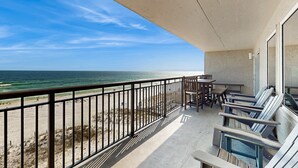Un balcone con vista sulla spiaggia e sull'oceano. Sul balcone ci sono sedie e tavoli.