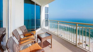 A balcony with wicker furniture, a glass table, and a view of the ocean. - 13th-floor condo with amazing views, pools, gym & beach access (Perdido Key)