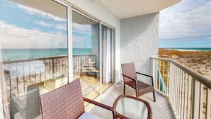 A balcony with wicker furniture, a glass door leading to a beach view, and a white textured wall. - Cozy beachfront condo, beach setup included, pool, quick drive to dining (Fort Walton Beach)