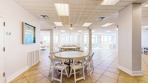 A spacious, well-lit meeting room with a large round table and white chairs, large windows, and a tiled floor. - Cozy beachfront condo, beach setup included, pool, quick drive to dining (Fort Walton Beach)