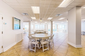 A spacious, well-lit meeting room with a large round table and white chairs, large windows, and a tiled floor.