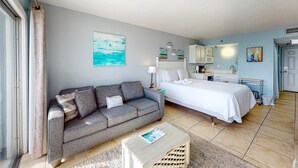 A compact bedroom with a bed, a sofa, a small table, and a kitchenette. - Cozy beachfront condo, beach setup included, pool, quick drive to dining (Fort Walton Beach)