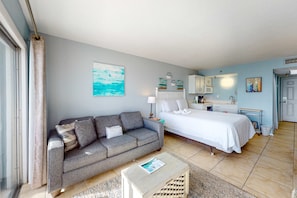 A compact bedroom with a bed, a sofa, a small table, and a kitchenette.