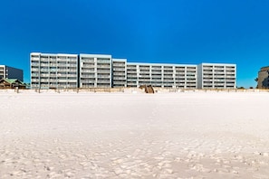A beachfront hotel with multiple floors, balconies, and a sandy beach in the foreground.