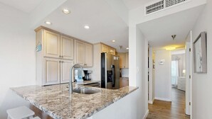A kitchen with granite countertops, stainless steel appliances, and white cabinetry. - Beautiful condo in beachfront building with pool, balcony, AC & lovely decor (Fort Walton Beach)