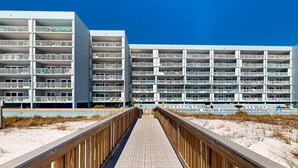 A modern hotel with multiple balconies and a wooden boardwalk leading to the beach. - Beautiful condo in beachfront building with pool, balcony, AC & lovely decor (Fort Walton Beach)
