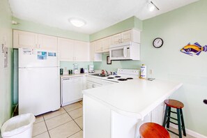 A kitchen with white cabinets, a microwave, a stove, and a sink. There is a clock on the wall and a fish decal. - Beachfront Condo w/ Gulf View, Balcony, WiFi & Shared Outdoor Pool/Gym (Perdido Key)