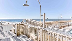 Ein hölzerner Steg mit einem Metall-Lampenpfosten und einem Tor, der zu einem Strand mit blauem Himmel führt.