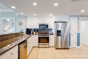 A modern kitchen with white cabinets, stainless steel appliances, granite countertops, and a tiled floor. - Beachside condo with a pool, hot tub, washer/dryer, beach access - snowbirds OK (Panama City Beach)