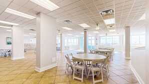 Un vaste espace intérieur doté d’un haut plafond, d’un sol carrelé et de nombreuses tables et chaises disposées pour les repas ou les réunions.