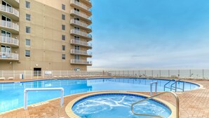 A swimming pool area with a hot tub, surrounded by a brick patio and a high-rise building with balconies. - 6th-floor Gulf & beachfront condo with pools, hot tubs, restaurant, & game room (Panama City Beach)