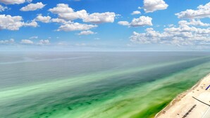 A beach with clear turquoise waters, a sandy shore, and a clear sky with scattered clouds. - 6th-floor Gulf & beachfront condo with pools, hot tubs, restaurant, & game room (Panama City Beach)