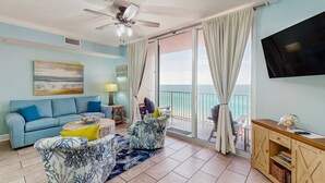 A living room with a sofa, armchairs, a coffee table, a TV, and a balcony with curtains. - 6th-floor Gulf & beachfront condo with pools, hot tubs, restaurant, & game room (Panama City Beach)