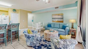 A living room with a blue sofa, a round coffee table, and a ceiling fan. - 6th-floor Gulf & beachfront condo with pools, hot tubs, restaurant, & game room (Panama City Beach)