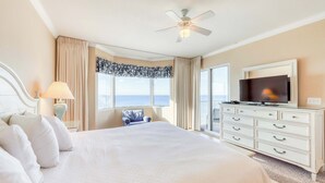 Een hotelkamer met een groot bed, een televisie, een plafondventilator en uitzicht op de oceaan.