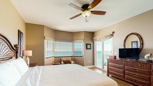 A bedroom with a large bed, a ceiling fan, a dresser, a television, and a window with blinds. - Exclusive Gulf-front condo | panoramic views | Pools & Hot tub (Panama City Beach)