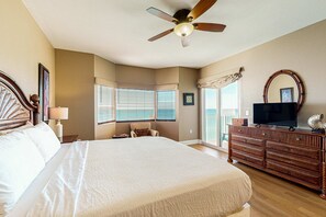 A bedroom with a large bed, a ceiling fan, a dresser, a television, and a window with blinds. - Exclusive Gulf-front condo | panoramic views | Pools & Hot tub (Panama City Beach)