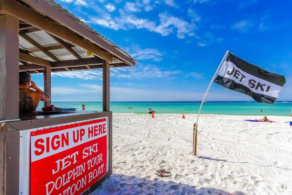 Une plage avec un panneau indiquant la présence de jet-skis et un tableau d’inscription pour les excursions d’observation des dauphins.