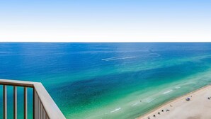 Uitzicht op een strand met helderblauw water en een zandstrand vanaf een balkon.