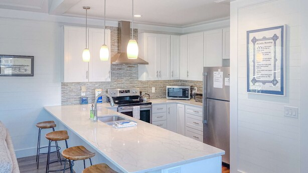 Una cocina moderna con armarios blancos, una isla de mármol, electrodomésticos de acero inoxidable e iluminación colgante.