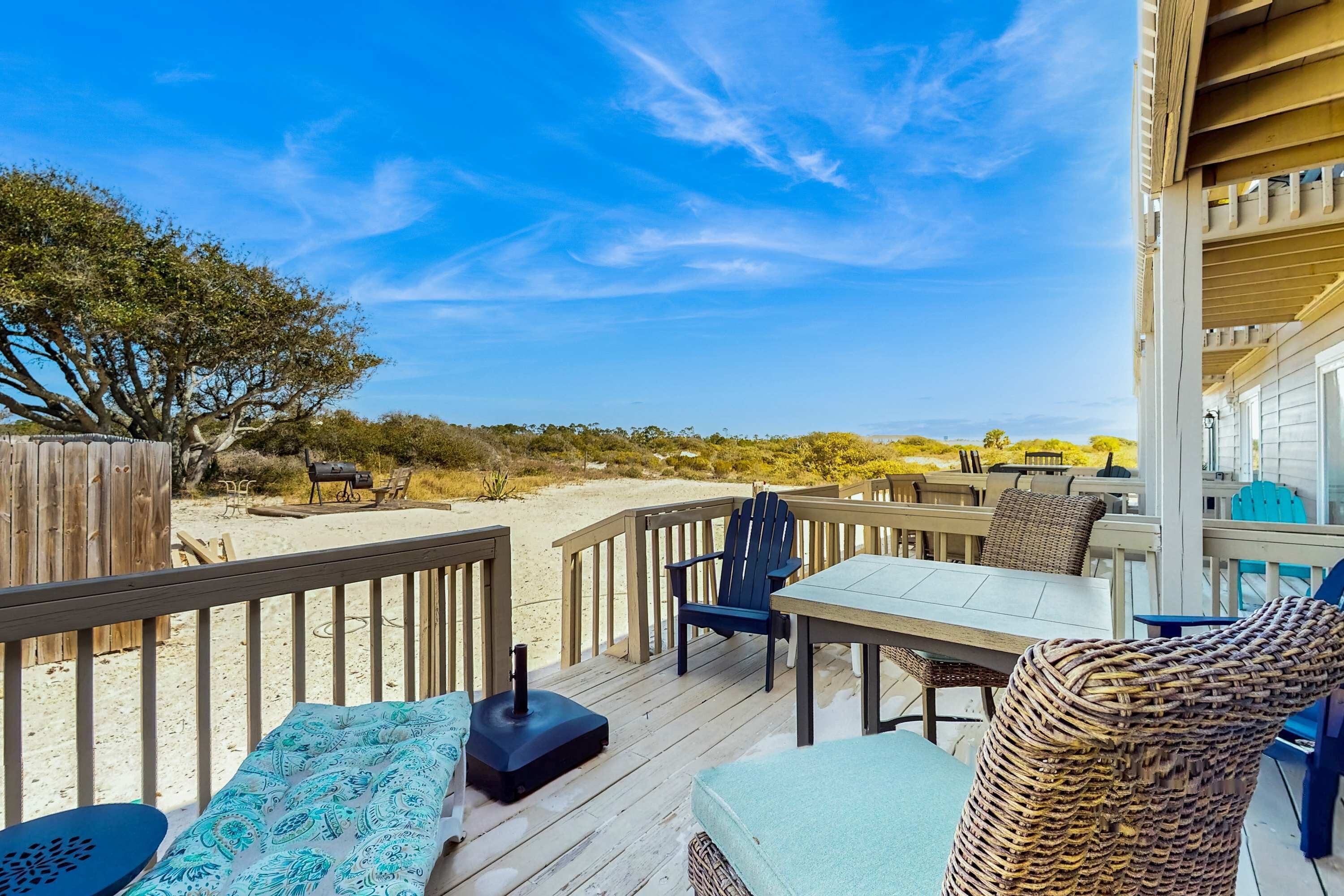 Una terraza con mobiliario exterior, una mesa y una silla, con vista a una playa arenosa y dunas.