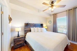 A bedroom with a wooden headboard, a bed with white bedding, a nightstand with a lamp, and a ceiling fan. - Gulf-front condo with amazing beach views, 3 pools, hot tubs, balcony, gym & AC (Panama City Beach)