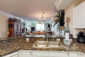 A kitchen with granite countertops, a double sink, and a dining area with wicker furniture. - Gorgeous gulf-front location & resort pools, beach service, and hot tubs (Panama City Beach)