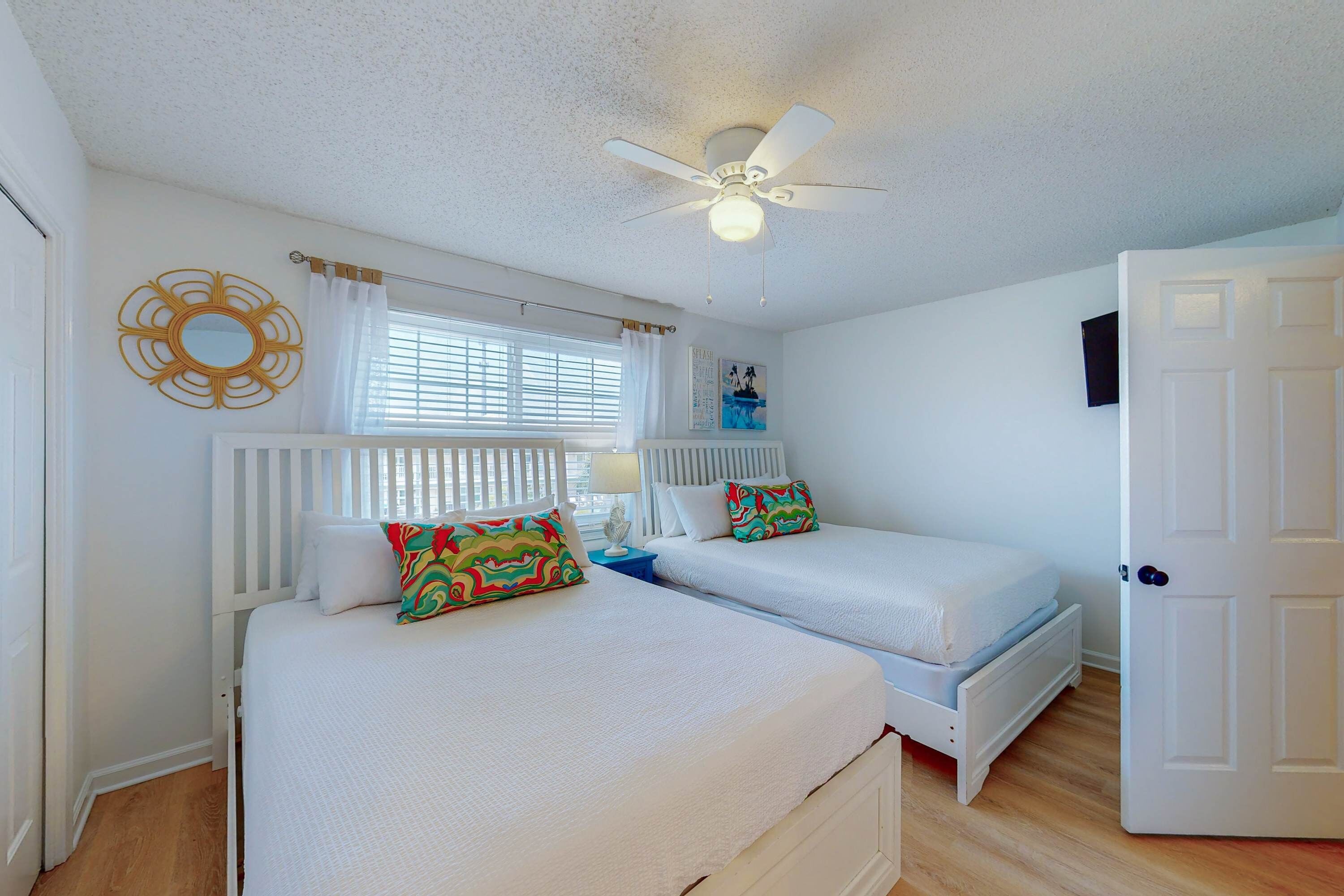A bedroom with two beds, a ceiling fan, a window with blinds, and a white door.