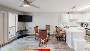 A modern kitchen with white cabinets, a dining area with wicker chairs, a glass-top table, and a ceiling fan. - Updated condo with balcony, central AC, pools, hot tub, grills, & beach access (Perdido Key)