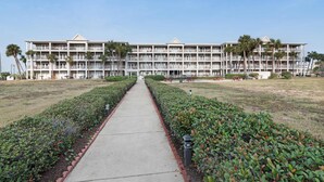 A multi-story hotel with a central courtyard, surrounded by manicured lawns and palm trees. - Updated condo with balcony, central AC, pools, hot tub, grills, & beach access (Perdido Key)