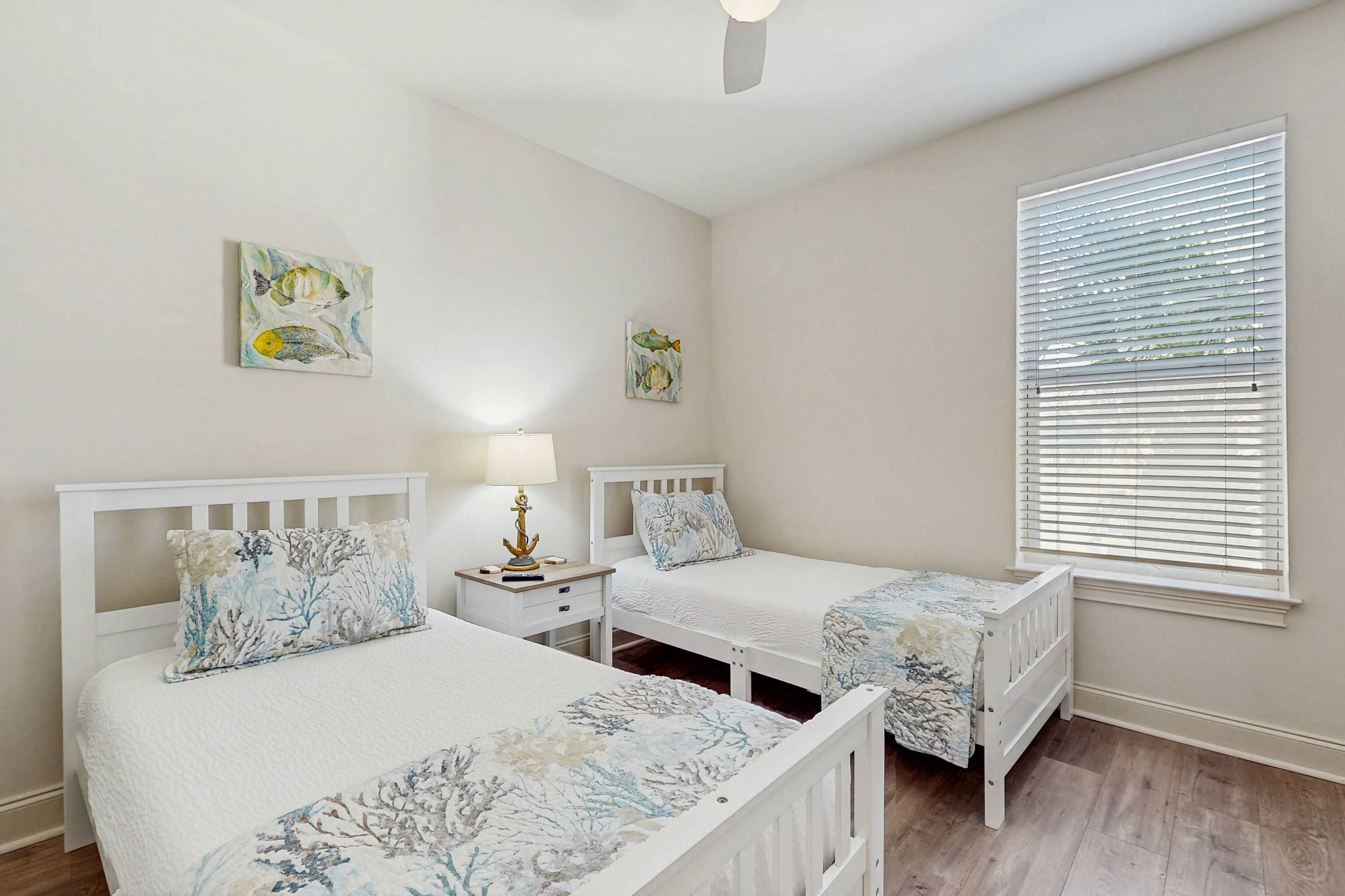 A bedroom with two single beds, a nightstand with a lamp, and a window with blinds.