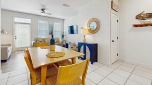 Uma sala de jantar com uma mesa e cadeiras de madeira, um ventilador de teto e uma televisão na parede.