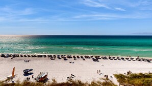 Une plage bordée de rangées de chaises longues et de parasols, une tour de surveillance pour les sauveteurs, et une vue dégagée sur l’océan.