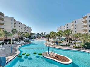 A swimming pool with lounge chairs and palm trees, surrounded by multi-story buildings. - Ground-Floor Condo At Waterscape Waterfall, Lazy River, Beach Chairs (Fort Walton Beach)
