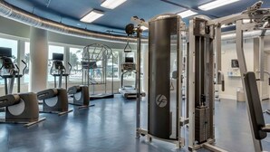 Een sportschool met diverse fitnessapparaten, grote ramen en een plafond met blootliggende buizen.