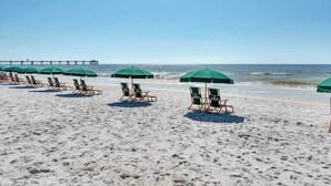 Een strand met rijen strandstoelen en groene parasols, een pier op de achtergrond en de oceaan.