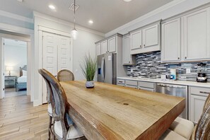 Une cuisine moderne avec des meubles blancs, une table à manger en bois et un réfrigérateur.