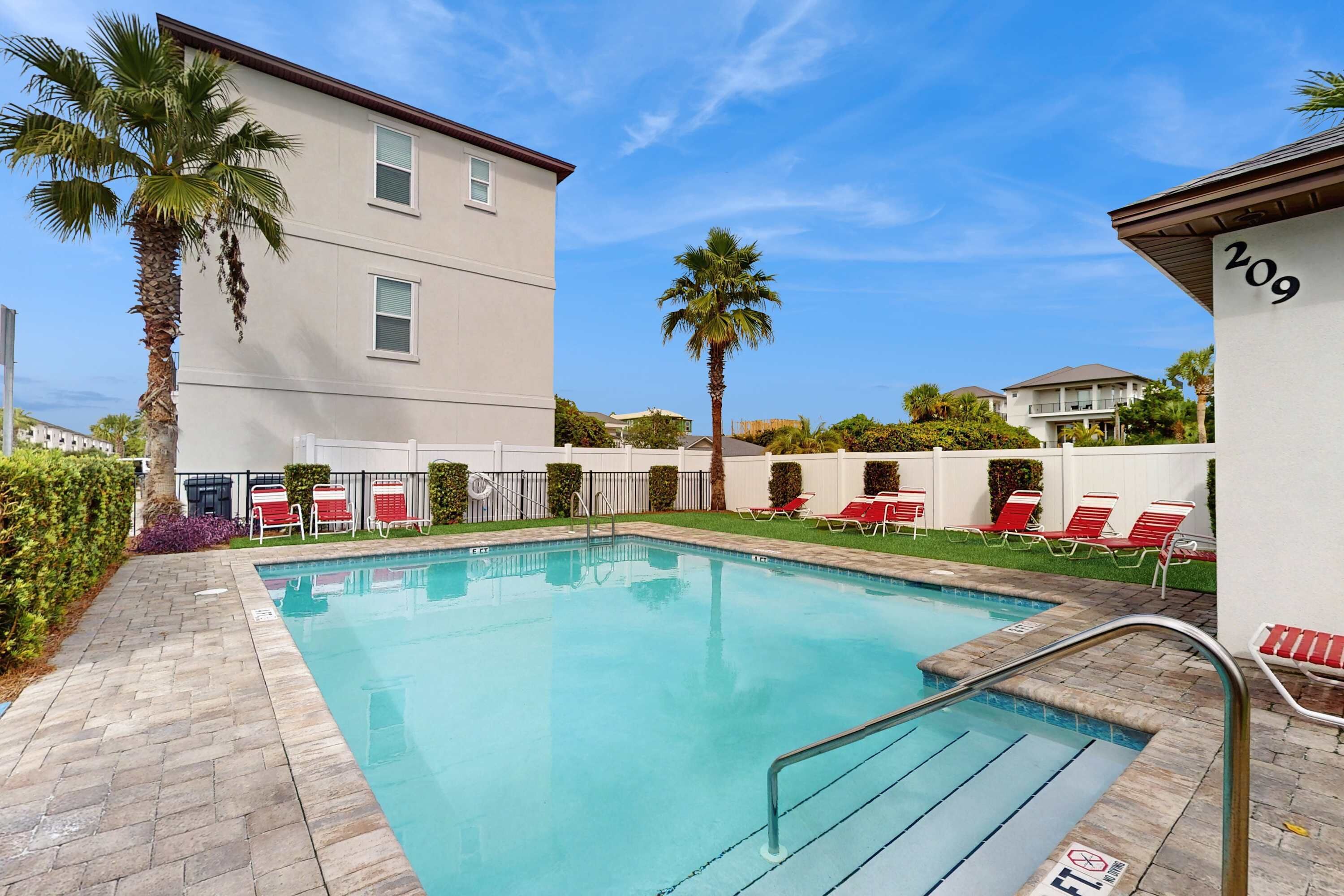 A swimming pool with red lounge chairs, palm trees, and a building with the number 209.